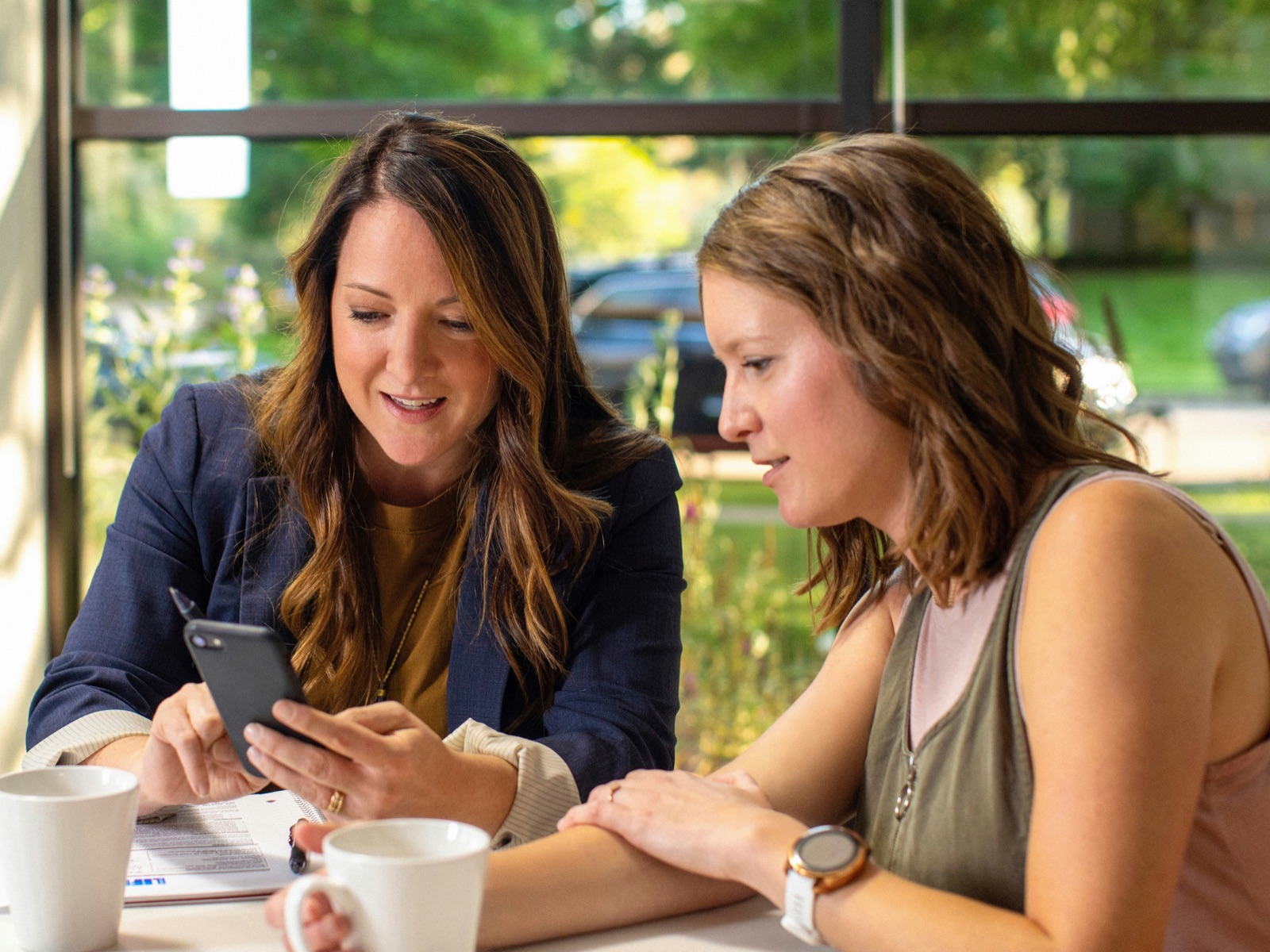 Two people leaning in over coffee, looking at something together on a phone